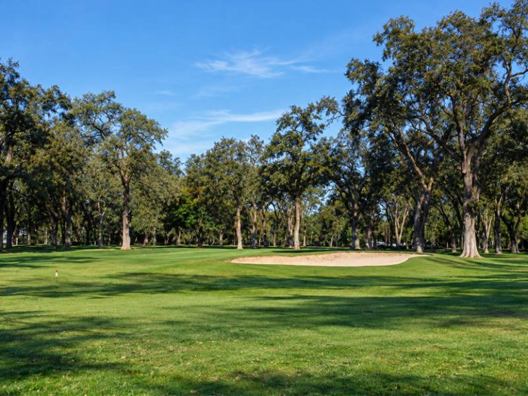 Fairway and greenside bunker at Plumas Lake Golf Club surrounded by mature oak trees.