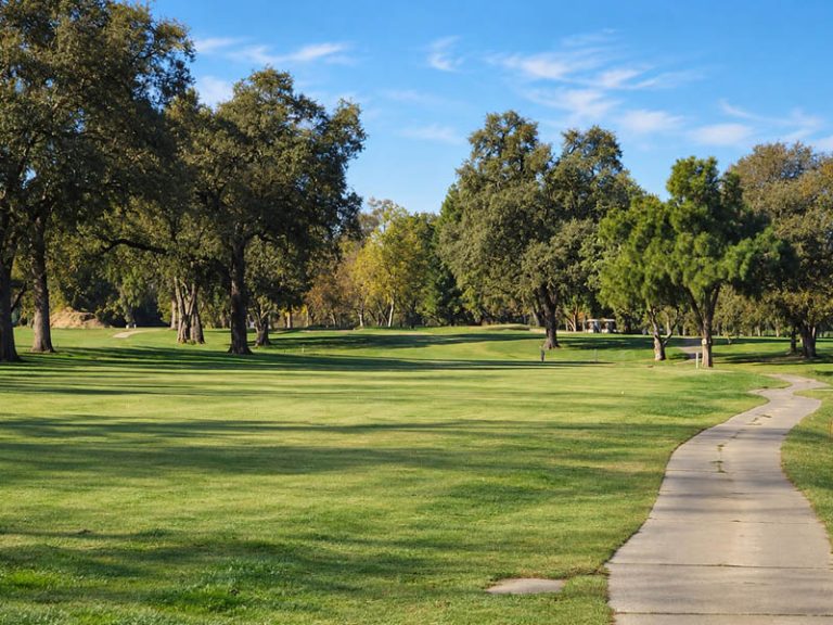 Golf course fairway and cart path at Plumas Lake Golf Club with trees lining both sides.