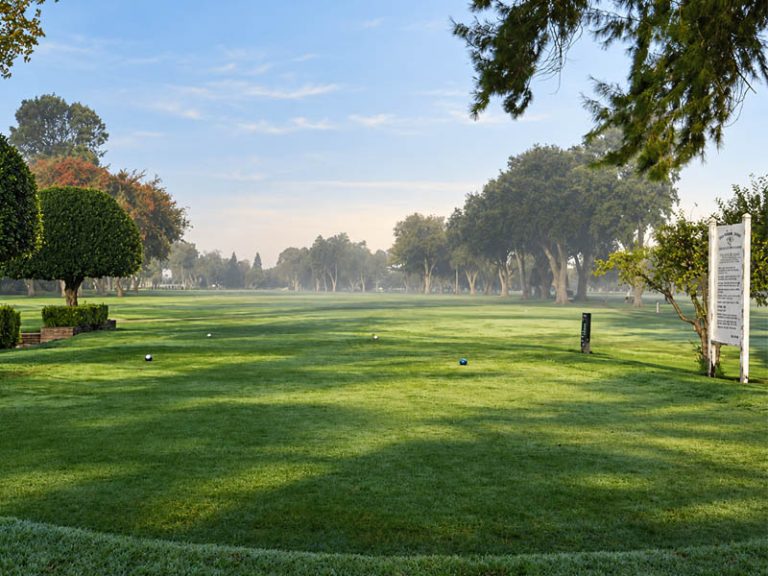 Tee box view at Plumas Lake Golf Club with mature trees framing a long fairway.