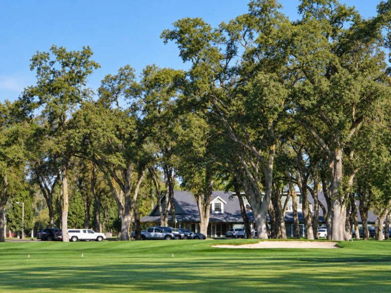 Clubhouse area at Plumas Lake Golf Club viewed across the fairway and mature oak trees.